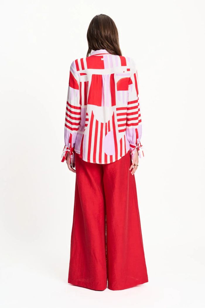 Back view of Pom Amsterdam SP9584 Sundeck Linen Blouse in bold red and pink geometric print with long sleeves, styled with red wide-leg pants. Shop Pom Amsterdam at Dotique.