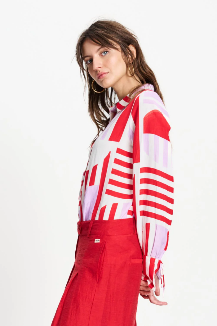 Model wearing Pom Amsterdam SP9584 Sundeck Linen Blouse with red and pink geometric print, styled with red pants. Shop Pom Amsterdam at Dotique.