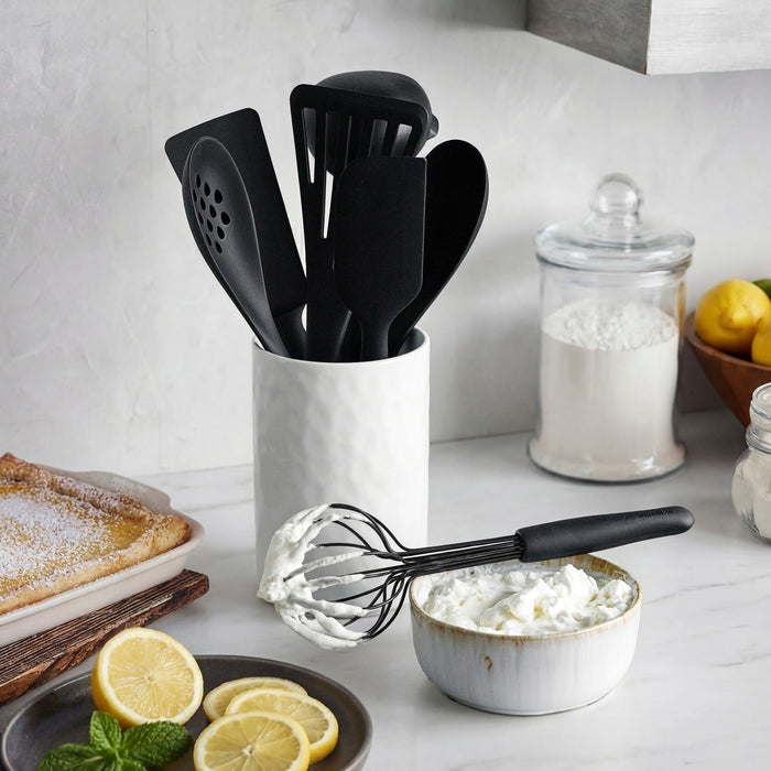 Black silicone 8-piece utensil and crock set with a whisk, next to lemons, mint, and a flour jar.