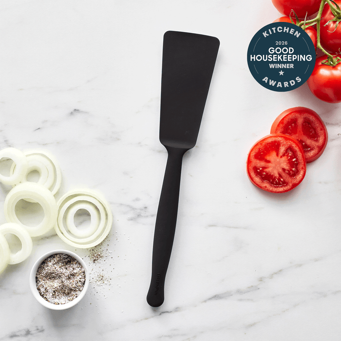 The Premiere Silicone Burger Turner in black rests on a marble countertop beside sliced onions, pepper, and tomatoes, with a 2016 Good Housekeeping Kitchen Winner Awards badge in the top right corner.