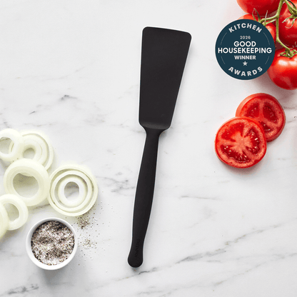 The Premiere Silicone Burger Turner in black rests on a marble countertop beside sliced onions, pepper, and tomatoes, with a 2016 Good Housekeeping Kitchen Winner Awards badge in the top right corner.