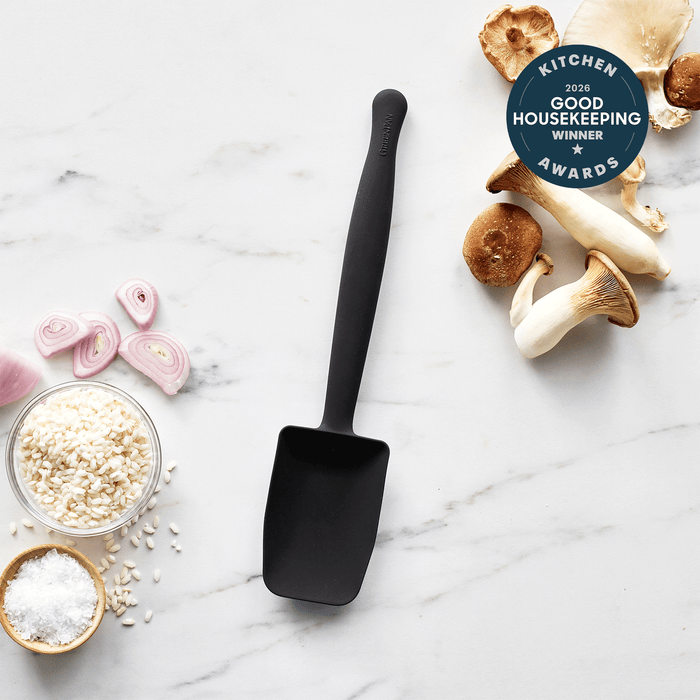 The Premiere Silicone Deep Sauté Spoon in black rests on white marble, surrounded by king oyster mushrooms, sliced shallots, risotto rice, and salt. This dishwasher-safe 2026 Good Housekeeping Kitchen Award winner is the perfect kitchen tool.