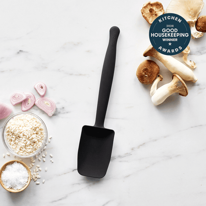 The Premiere Silicone Deep Sauté Spoon in black rests on white marble, surrounded by king oyster mushrooms, sliced shallots, risotto rice, and salt. This dishwasher-safe 2026 Good Housekeeping Kitchen Award winner is the perfect kitchen tool.