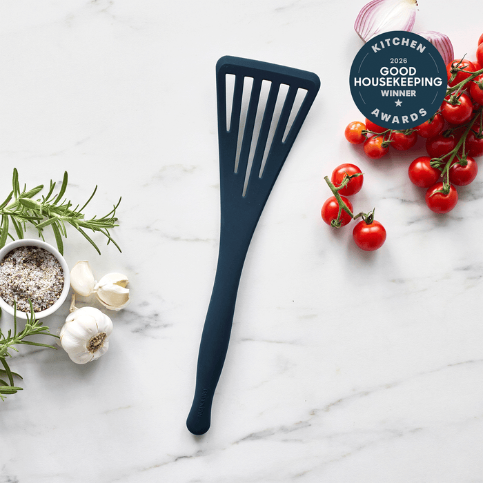 Oxford blue silicone fish turner on marble with garlic, rosemary, tomatoes, salt, and an award badge nearby.