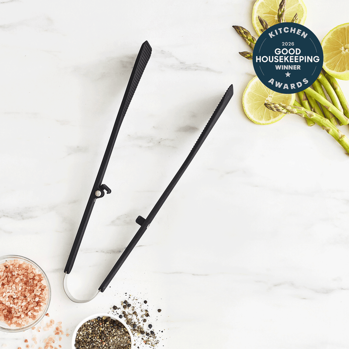 Premiere Silicone Wide Tongs | Black rest on a white marble surface near pink salt, pepper, asparagus, lemon slices, and a 2026 Good Housekeeping Kitchen Awards Winner badge. These heat-resistant tongs are ideal for any modern kitchen.