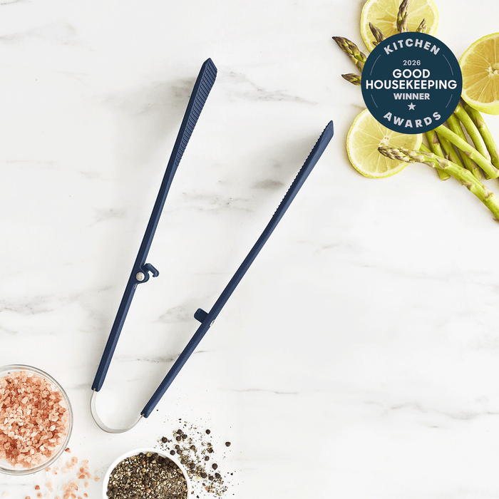 Blue silicone kitchen tongs with anti-slip grip on marble, surrounded by spices, asparagus, and lemon slices.