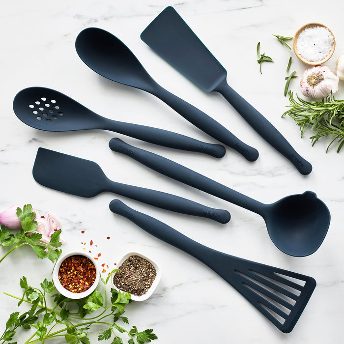 Silicone roasting scoop in Oxford Blue on marble, with herbs, spices, garlic cloves, and a small bowl of salt nearby.