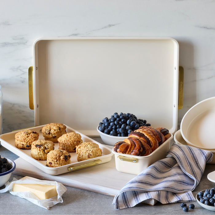 Scones, croissants, blueberries, and butter on a cream rectangular bakeware pan beside a striped towel.