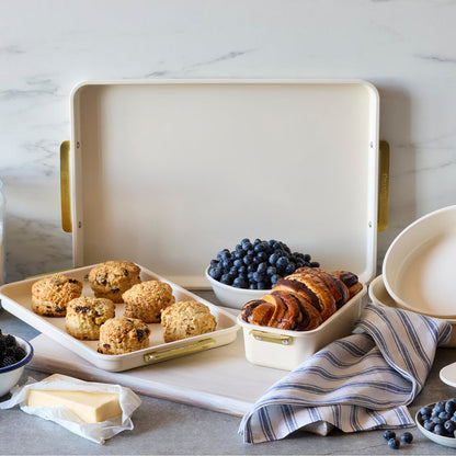 Scones, croissants, blueberries, and butter on a cream rectangular bakeware pan beside a striped towel.