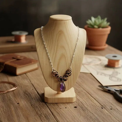 Silver and Copper Wire Sculpted Purple Crystal Drop Necklace displayed on a wooden bust with artistic materials in the background.