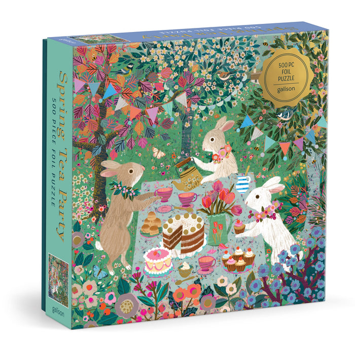 The Spring Tea Party 500 Piece Foil Puzzle by Victoria Ball features three rabbits at a whimsical tea party in a vibrant garden, surrounded by cakes, teacups, bunting, and blooming flowers.