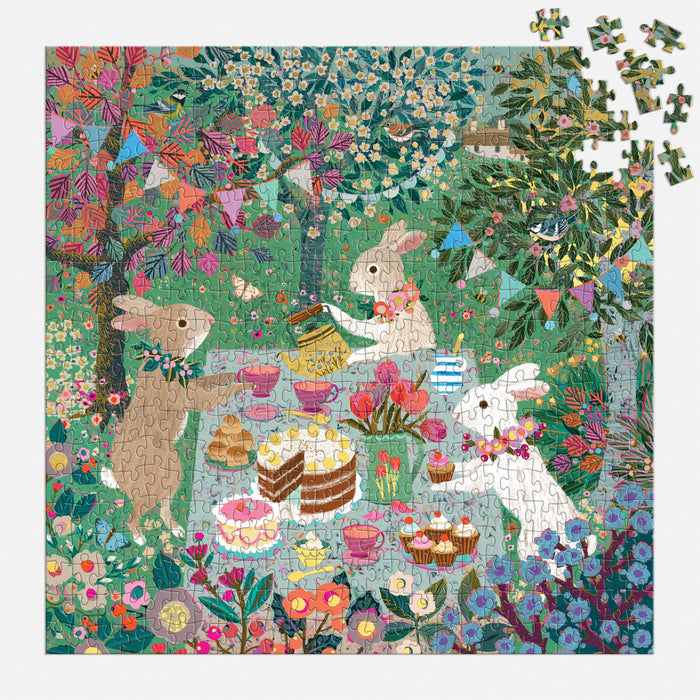 Three rabbits have a tea party with cakes and pastries in a vibrant garden on the Spring Tea Party 500 Piece Foil Puzzle by Victoria Ball. A few pieces are missing from the top right corner of this charming scene.