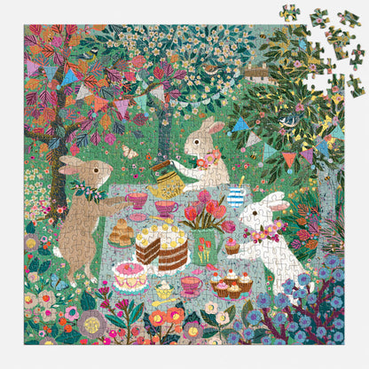 Three rabbits have a tea party with cakes and pastries in a vibrant garden on the Spring Tea Party 500 Piece Foil Puzzle by Victoria Ball. A few pieces are missing from the top right corner of this charming scene.