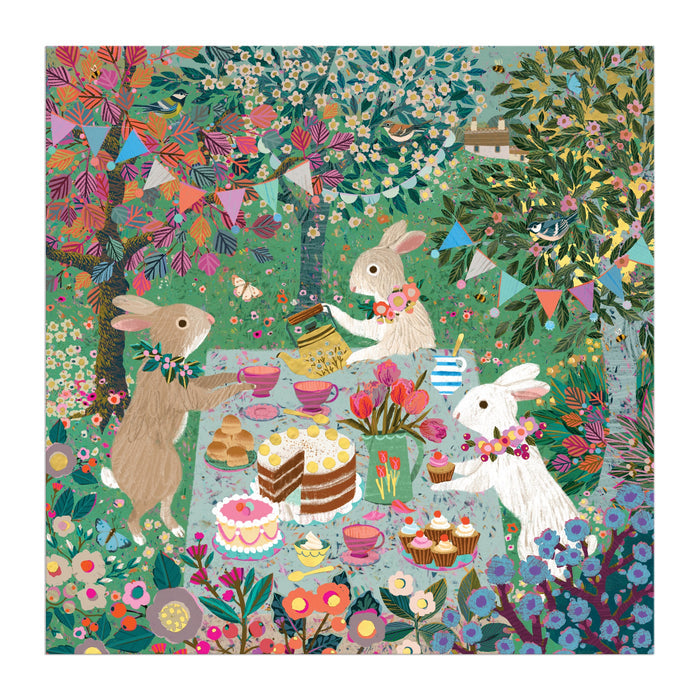 Three rabbits with flower garlands enjoy tea, cakes, and teacups at a festive table in a vibrant garden, surrounded by bunting and trees. Inspired by Victoria Ball art. Spring Tea Party 500 Piece Foil Puzzle by Victoria Ball.