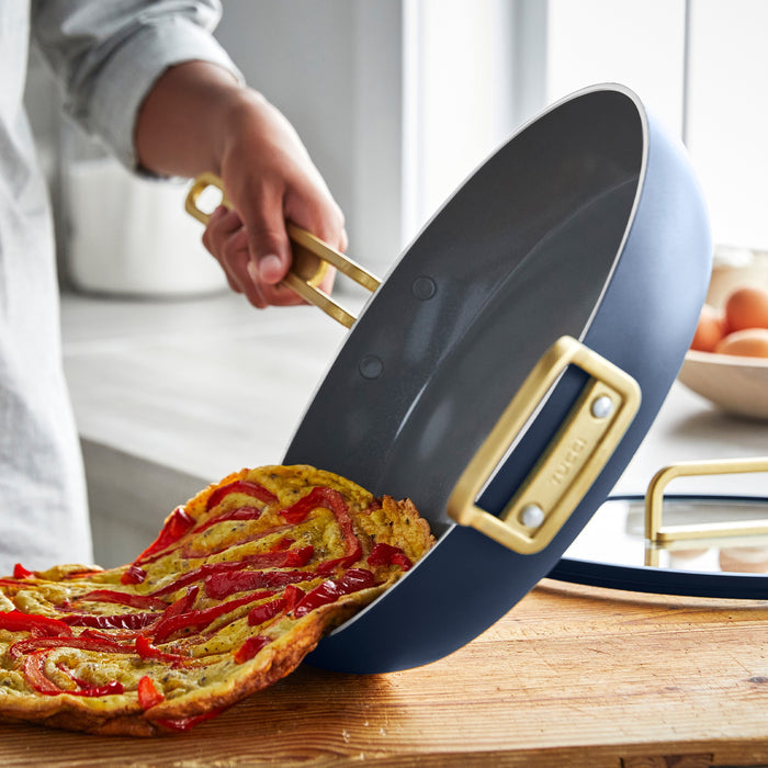 Red pepper omelette being slid from a blue Stanley Tucci 12-inch frypan onto a wooden board.