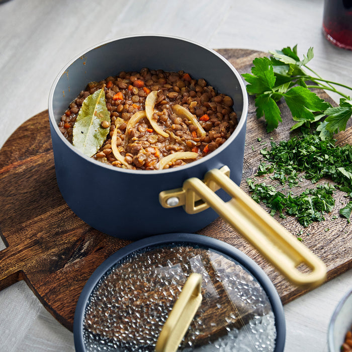 Blue ceramic nonstick saucepan with lid, filled with lentil stew, next to a pile of chopped parsley.