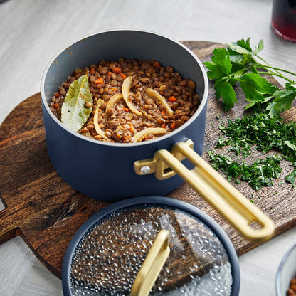Blue ceramic nonstick saucepan with lid, filled with lentil stew, next to a pile of chopped parsley.