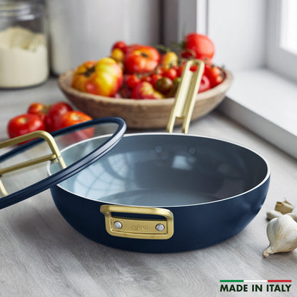 Marino Blue ceramic nonstick pan with glass lid beside fresh tomatoes and garlic on a counter.