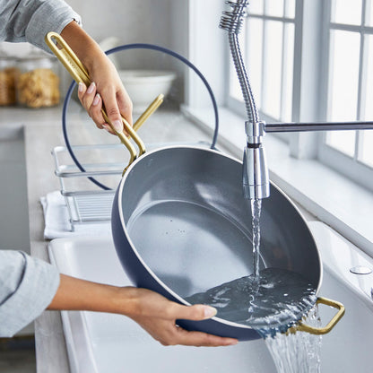 Blue ceramic nonstick pan being rinsed under running water in a bright kitchen sink.