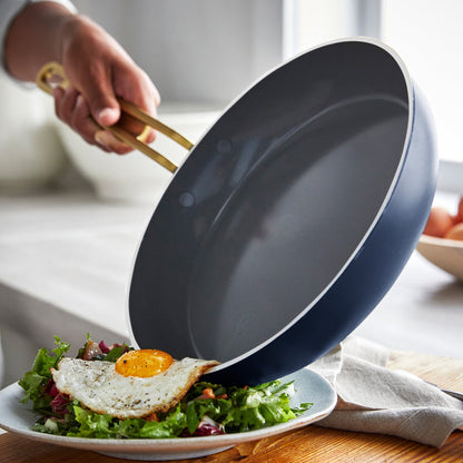 Hand tilting a ceramic nonstick frypan to slide a fried egg onto a plate of salad.