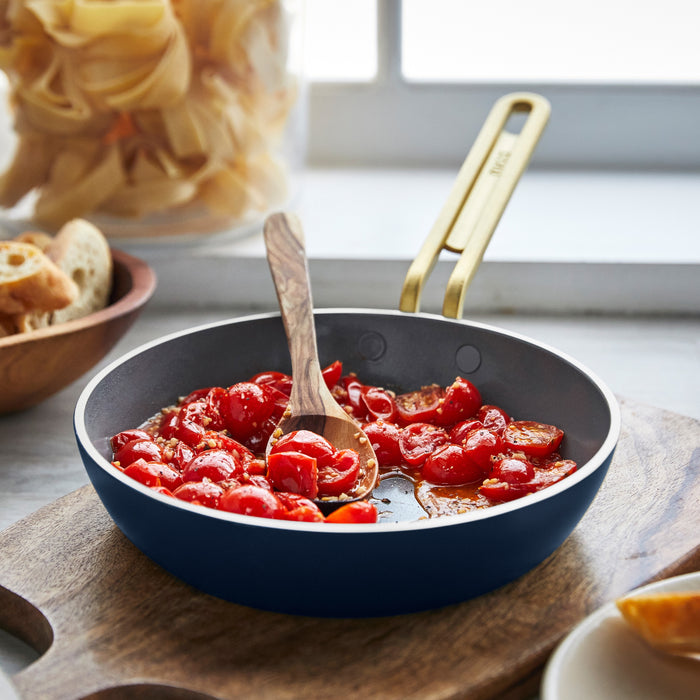 Marino Blue frypan set with cherry tomatoes and a wooden spoon displayed on a kitchen counter near a window.