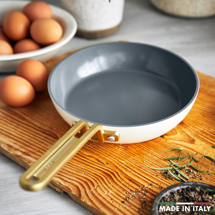 White ceramic nonstick 8-inch frypan with gold handle, eggs and fresh herbs beside it.