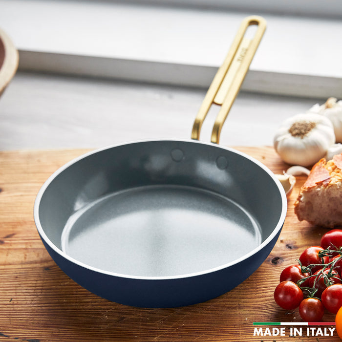 Ceramic nonstick 8-inch frypan in marino blue on a wooden counter with bread, garlic, and tomatoes nearby.