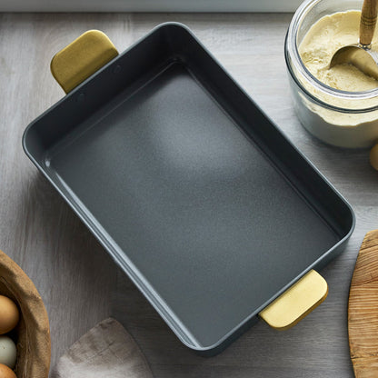 Venetian teal ceramic lasagna pan with gold handles on a kitchen counter next to baking ingredients.