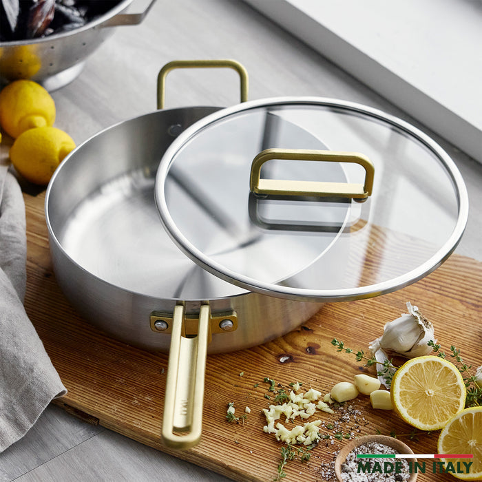 Gray 4-quart sauté pan with lid on a board, surrounded by garlic, lemon slices, and fresh herbs.