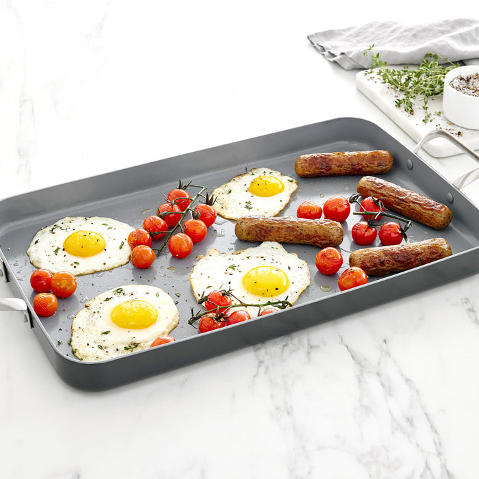 Fried eggs, tomatoes, and sausages on a gray ceramic double burner griddle.