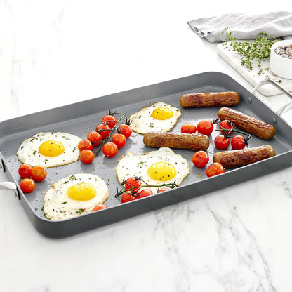 Fried eggs, tomatoes, and sausages on a gray ceramic double burner griddle.
