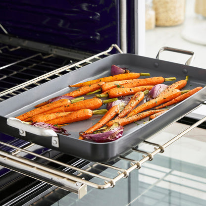 Chopped carrots and red onions on a gray ceramic nonstick griddle, ready for oven roasting.