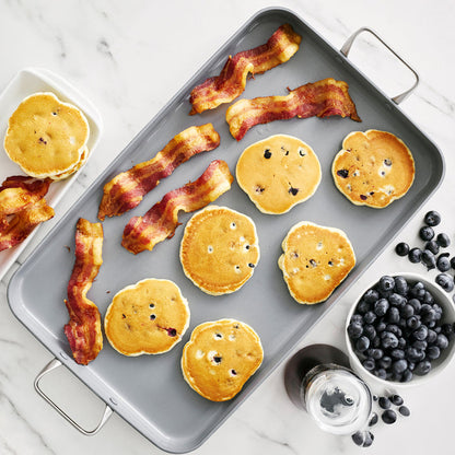 Ceramic nonstick griddle with bacon and blueberry pancakes; syrup and mixed berries on the side.