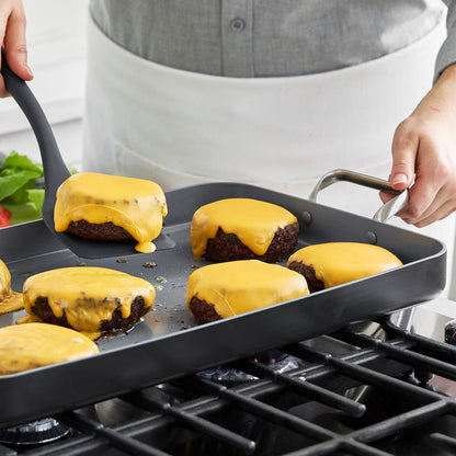 Cheeseburgers being cooked and flipped with a spatula on a large ceramic nonstick double burner griddle.